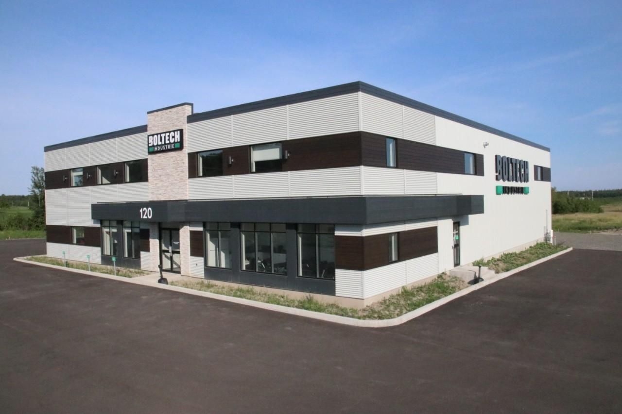 Vue aérienne de bâtiments commerciaux beiges avec parking, arbres et ciel bleu.