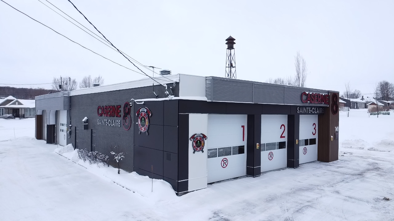 Caserne de pompiers avec trois portes de garage numérotées, dans un décor enneigé.