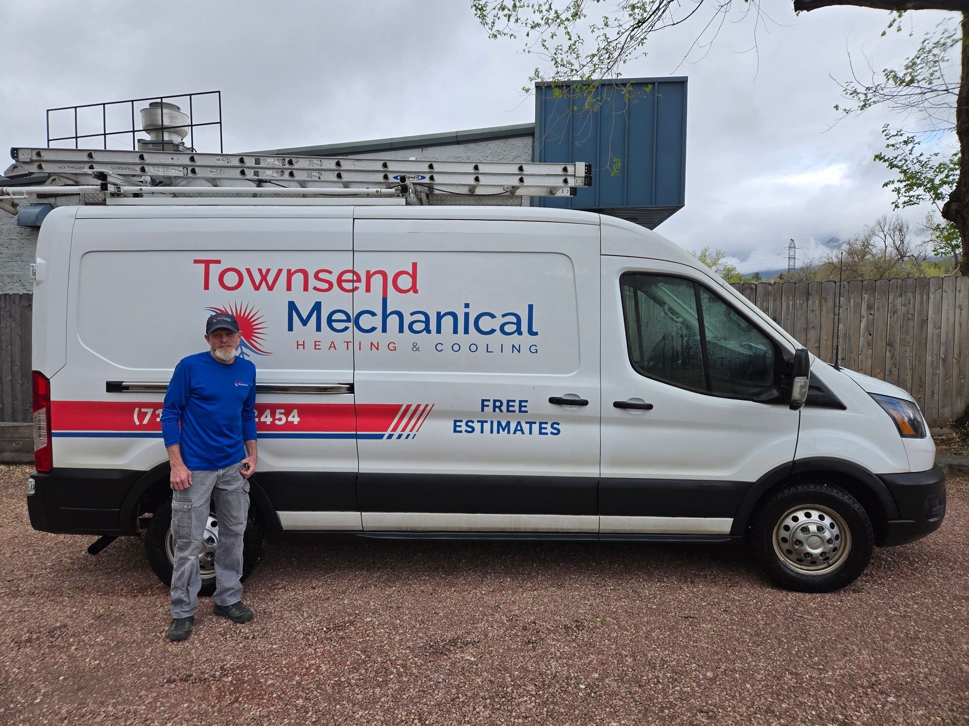 Man standing next to a white Townsend Mechanical service van. Van has ladder on top. Cloudy sky background.