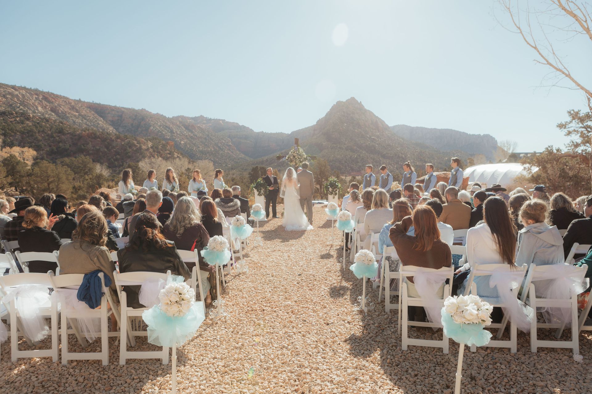 Outdoor wedding ceremony at Zion Glamping Adventures with a stunning mountain backdrop and rows of guests seated along aisle.