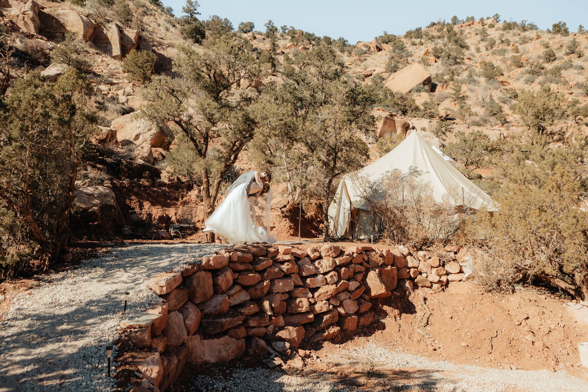 Bride and groom embracing in front of a glamping tent, set against the rugged landscape of Zion Glamping Adventures.