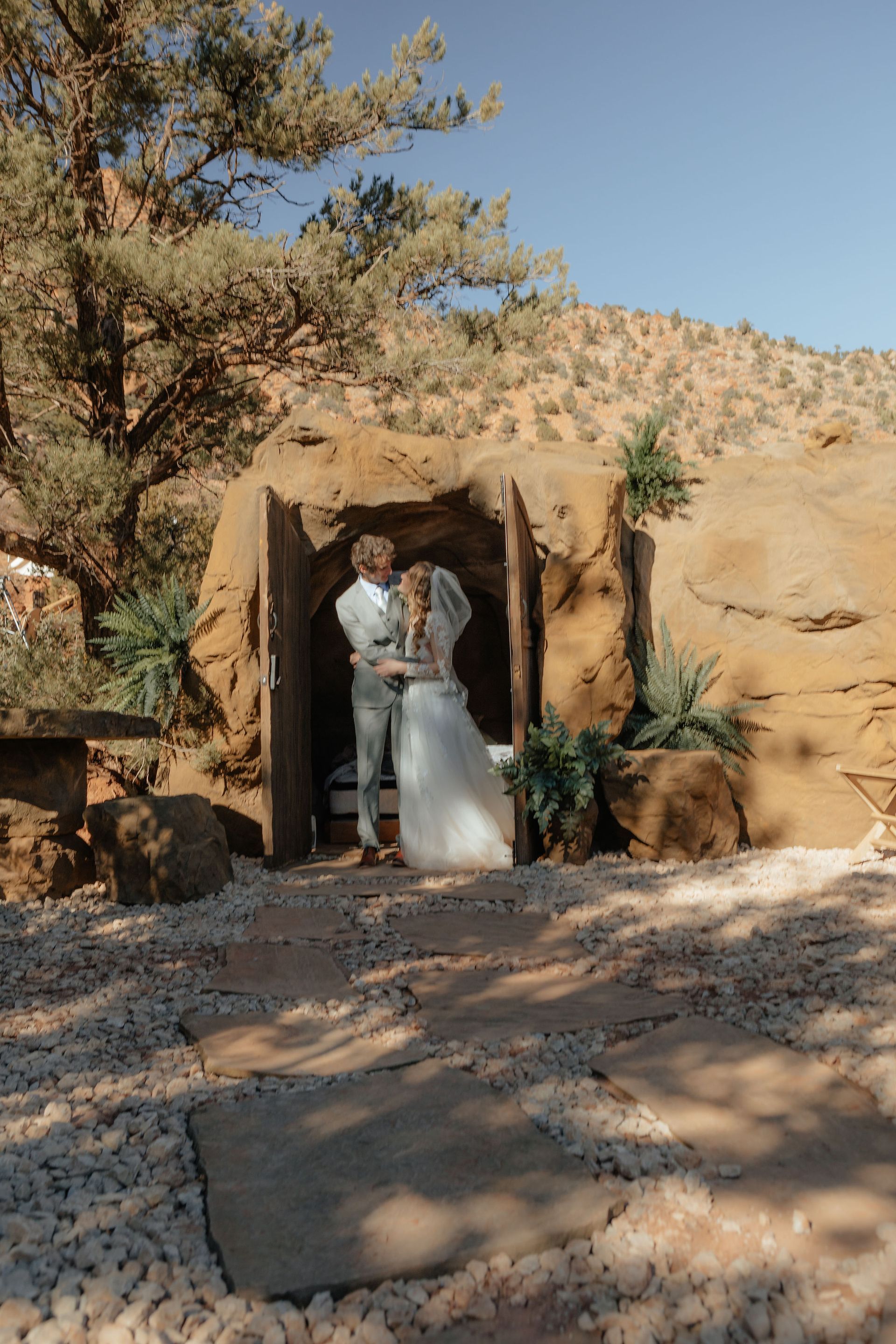 Bride and groom embracing in front of a Cave Room, set against the rugged landscape of Zion Glamping Adventures.
