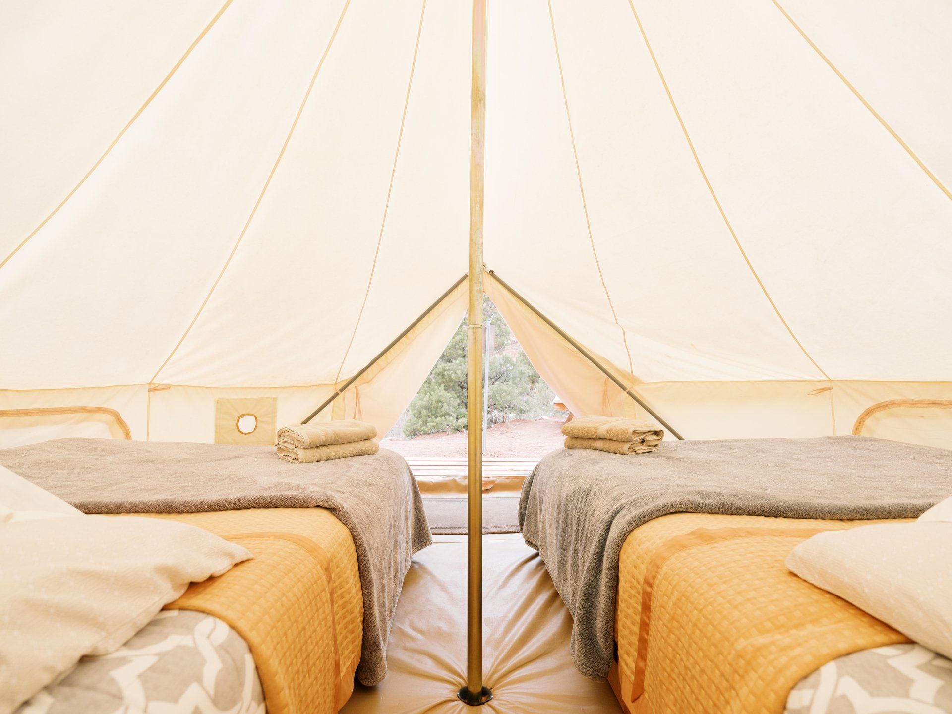 Glamping tent interior with two cozy beds, soft linens, and neatly folded towels, providing a comfortable space for guests.