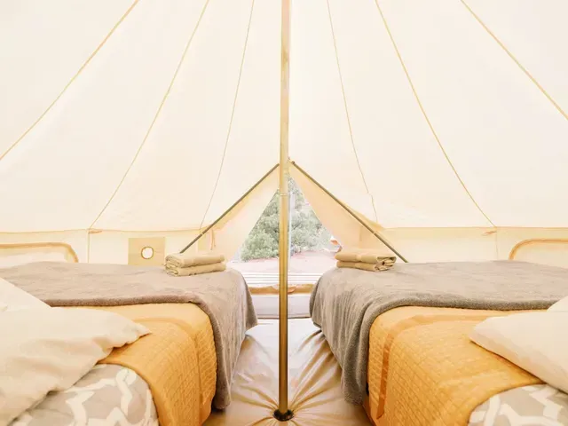 Inside view of a glamping tent with two beds neatly made and natural light coming through the entrance.