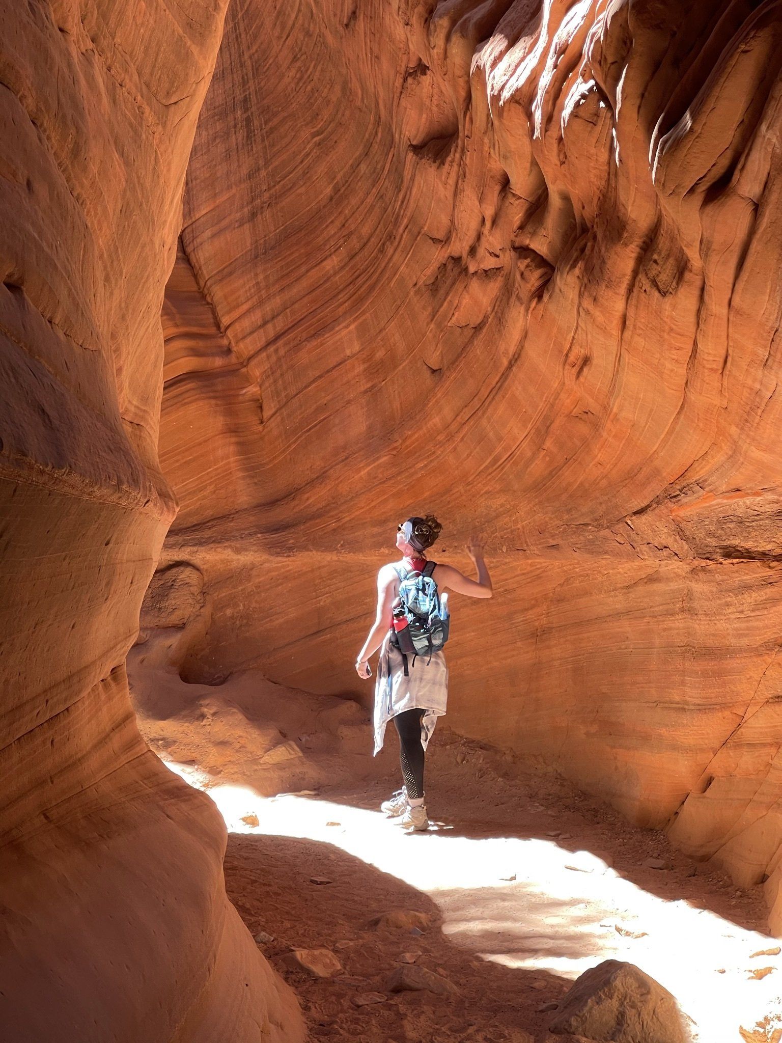 A woman exploring a narrow red rock canyon, sunlight filtering in from above.