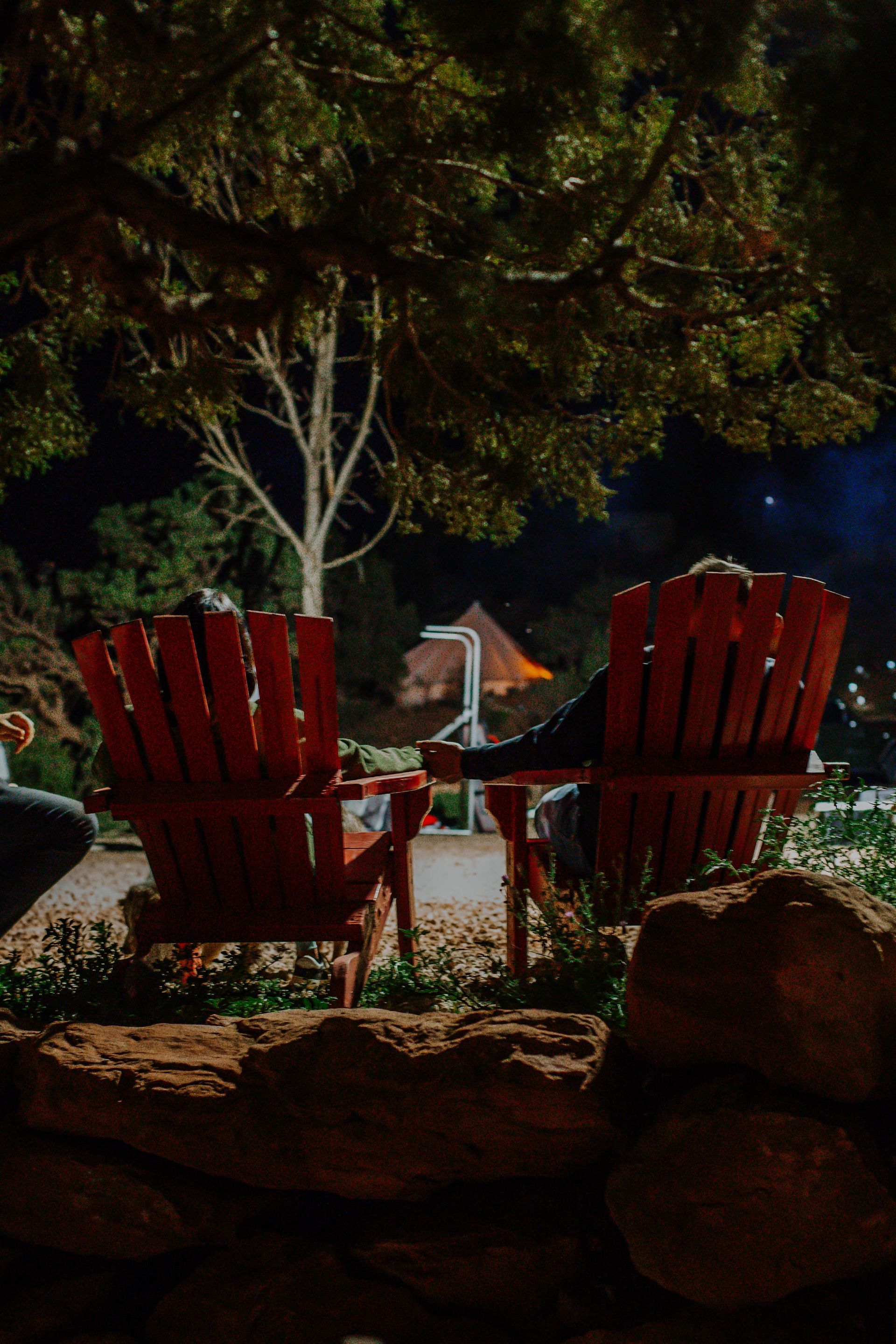 Guests relaxing in red Adirondack chairs under the night sky at Zion Glamping Adventures, surrounded by nature.