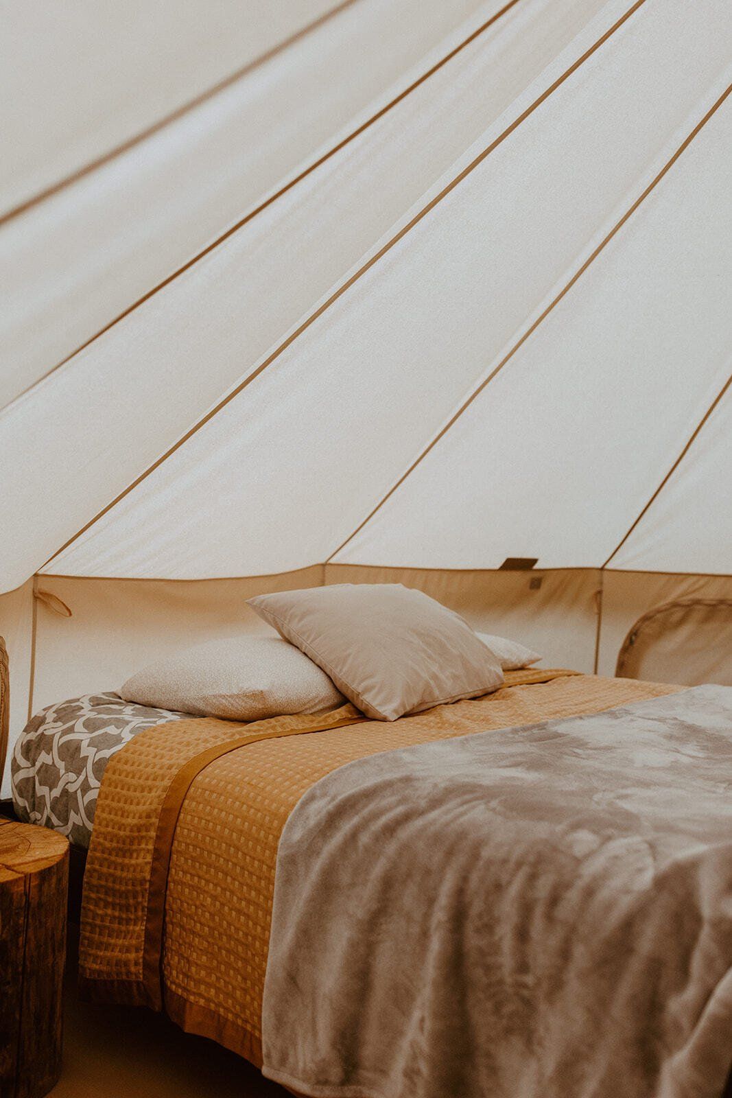 Comfortable bed inside a luxurious glamping tent, with neutral tones and cozy bedding, providing a peaceful retreat.