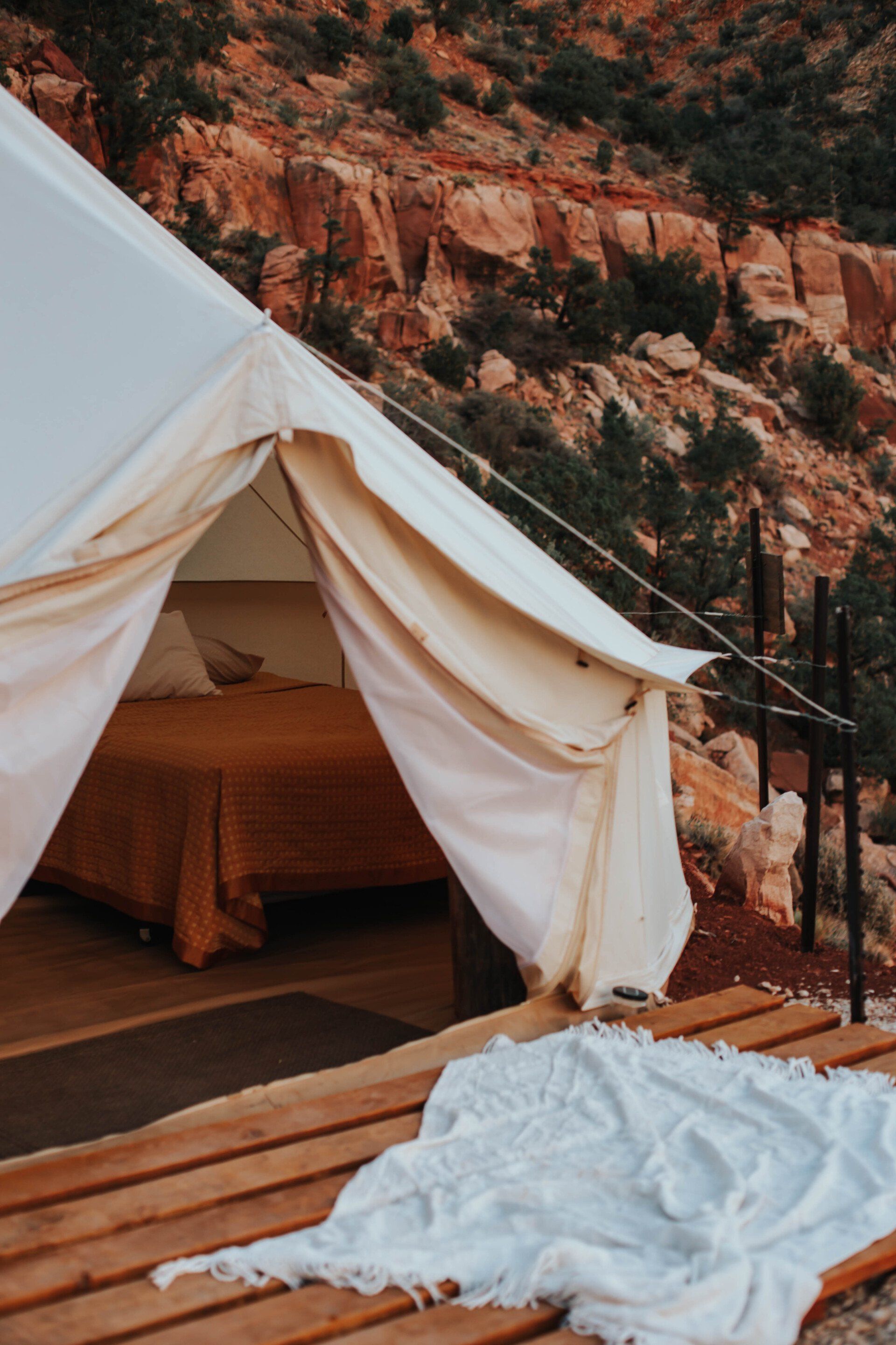 Glamping tent with an open entrance showcasing a comfortable bed and scenic outdoor surrounding, blending luxury with nature.