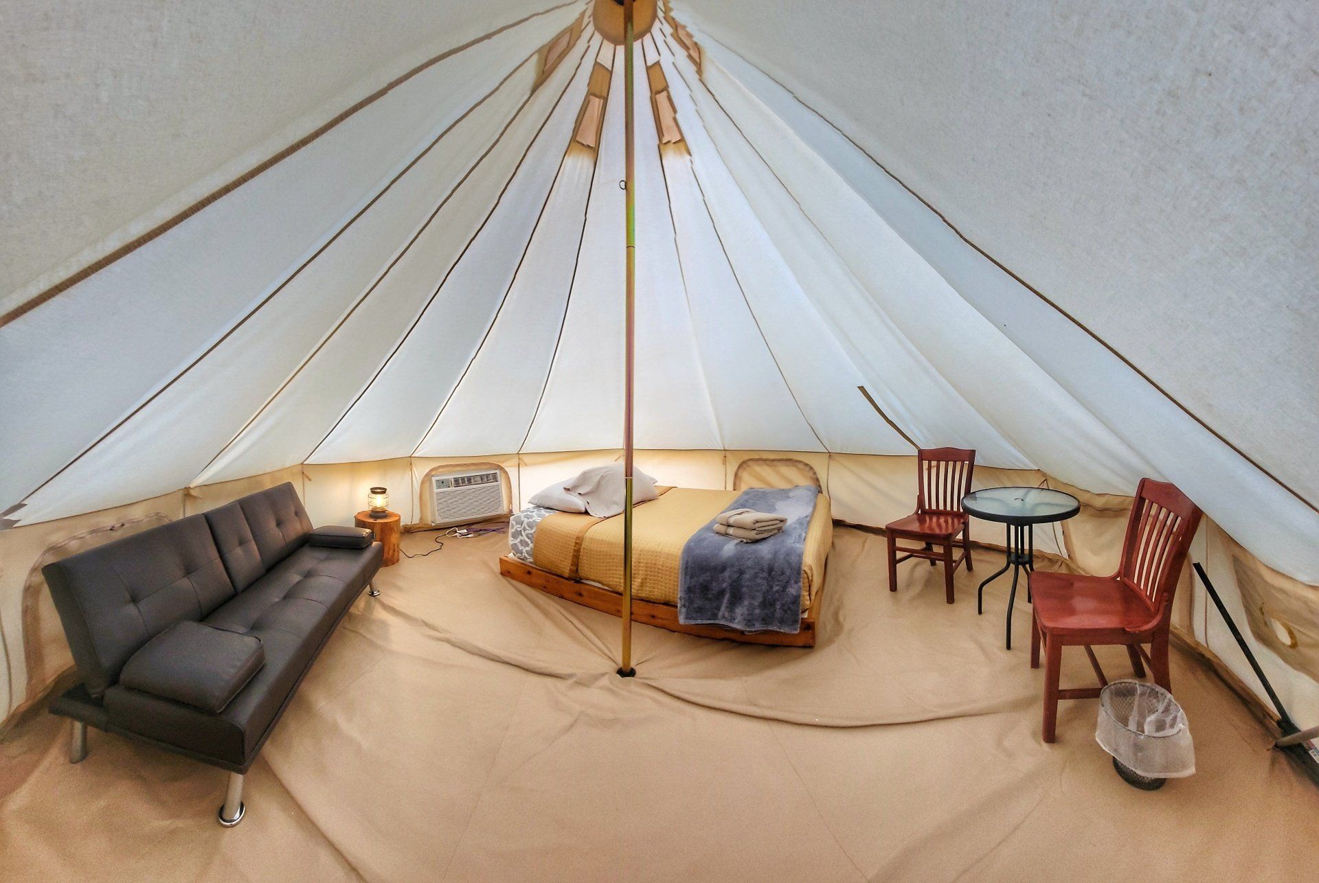 Interior of a spacious glamping tent featuring a comfortable bed, a sofa, and chairs, providing ample space.