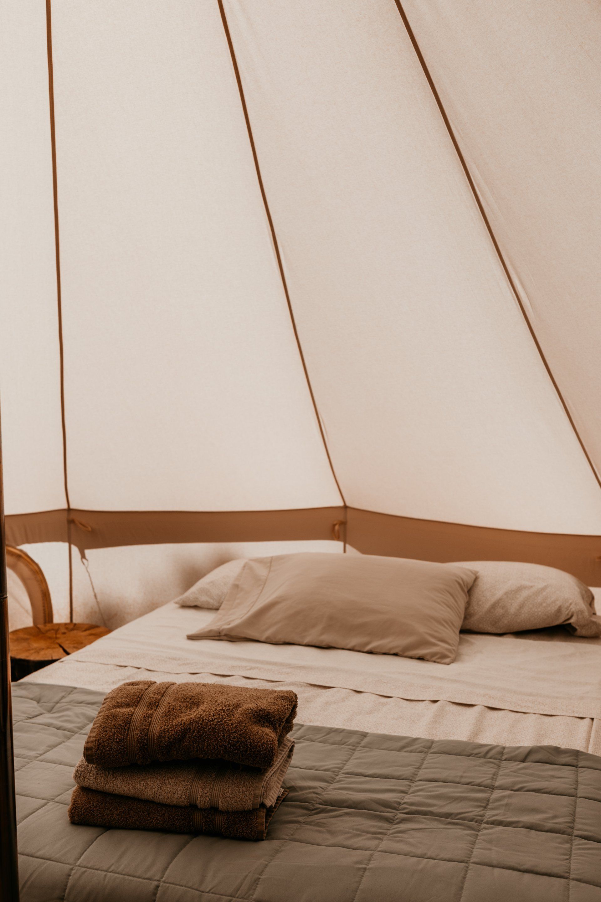 Close-up of a neatly made bed inside a glamping tent, with soft pillows, offering a clean and inviting space for guests.