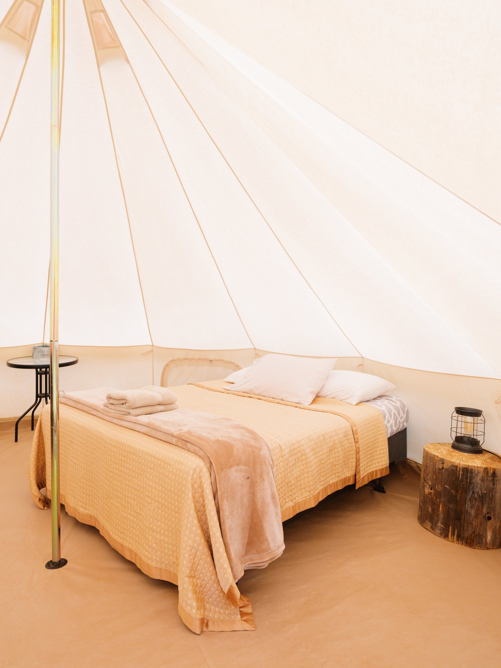 Spacious glamping tent interior with a comfortable bed, a small table, and natural light creating a serene ambiance.