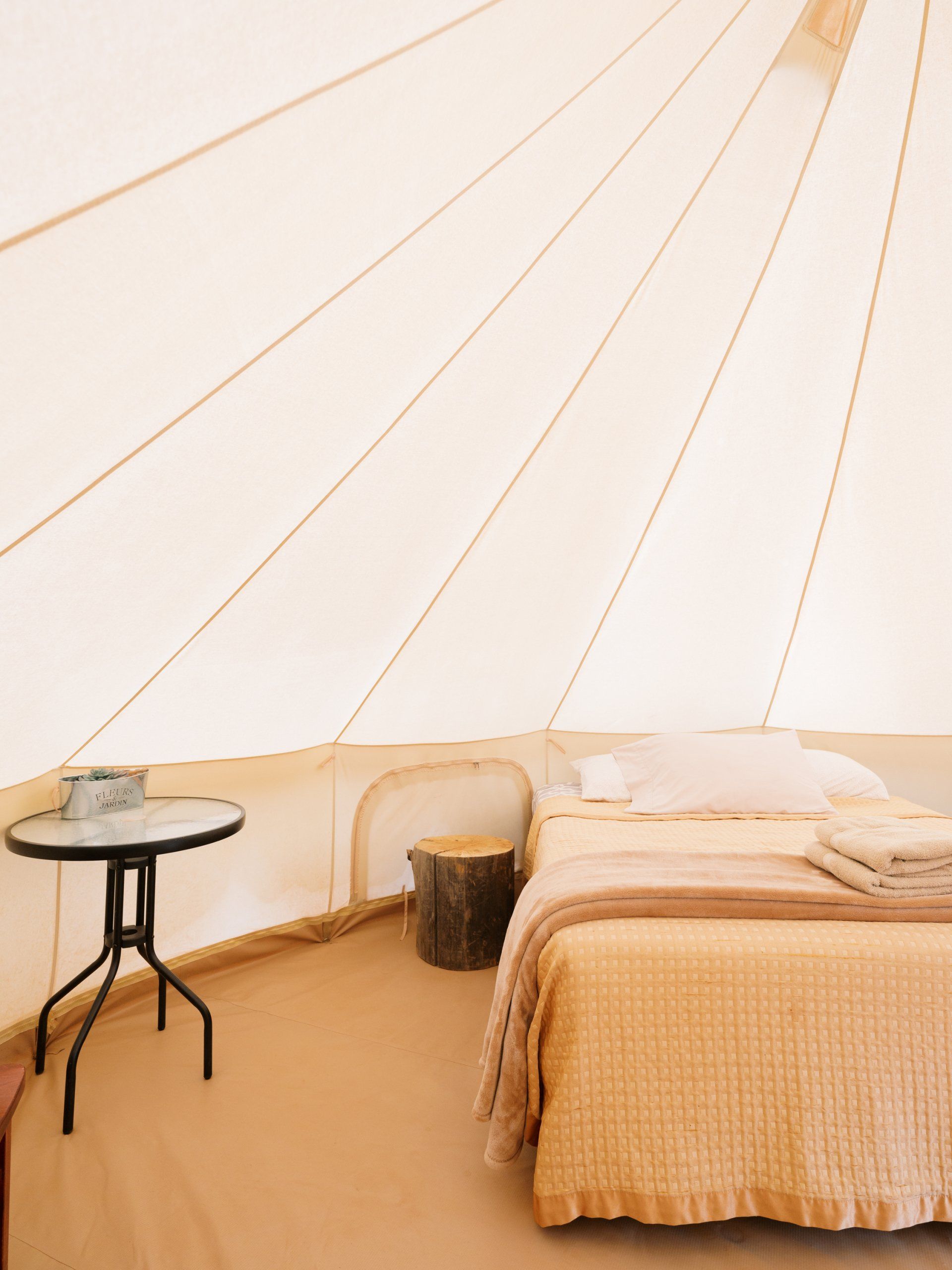 Interior of a glamping tent featuring a cozy bed with soft linens, an a side table, offering a relaxing atmosphere.