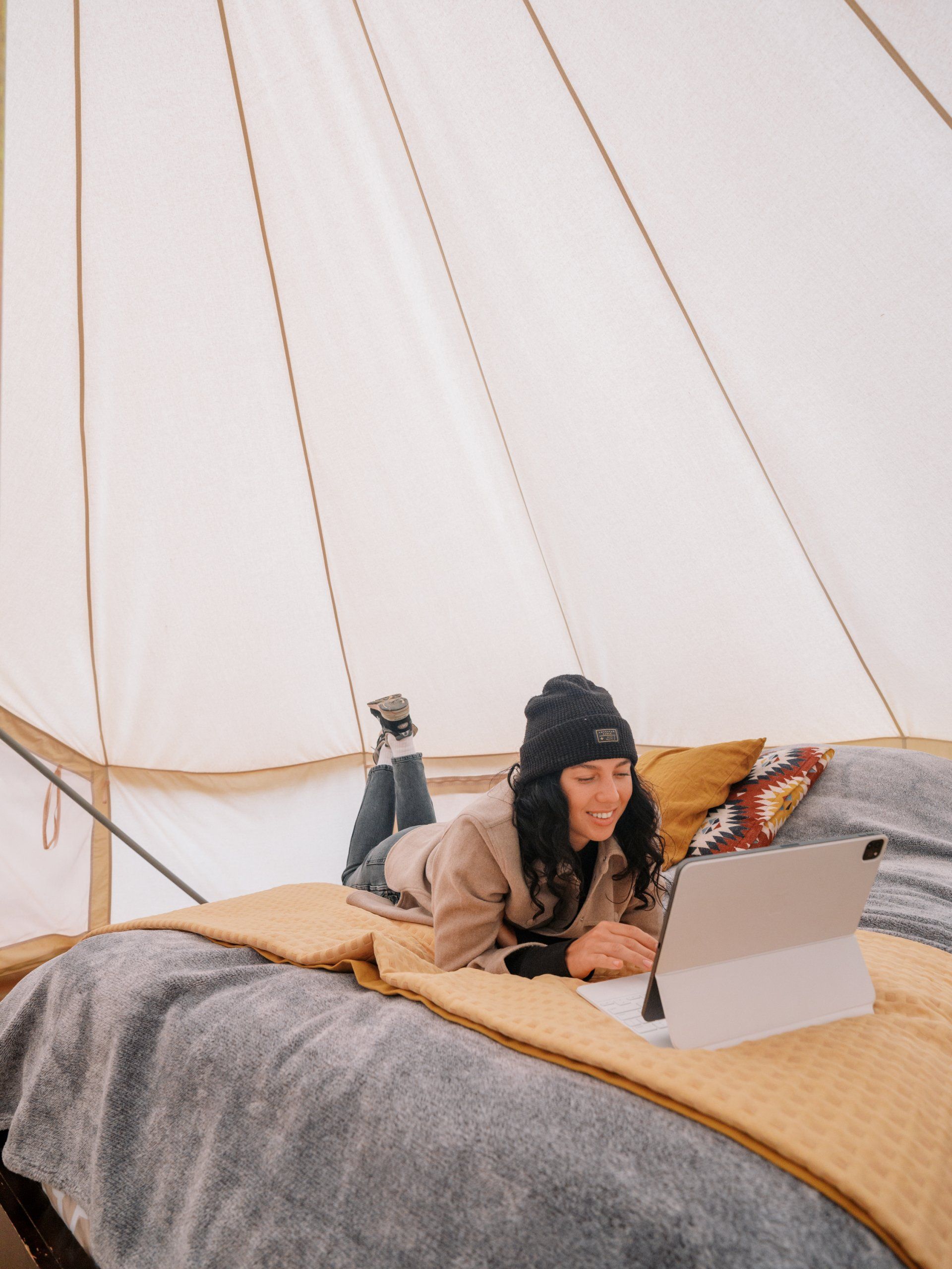 A guest relaxing on a bed inside a glamping tent, using a tablet, getting some work done at Zion Glamping Adventures