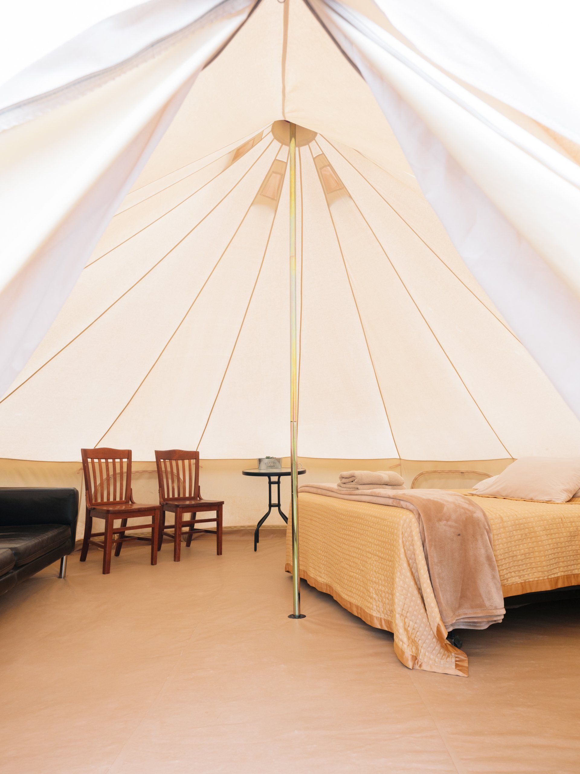 Spacious glamping featuring a comfortable bed, a small table, and chairs, offering a blend of comfort and natural ambiance.