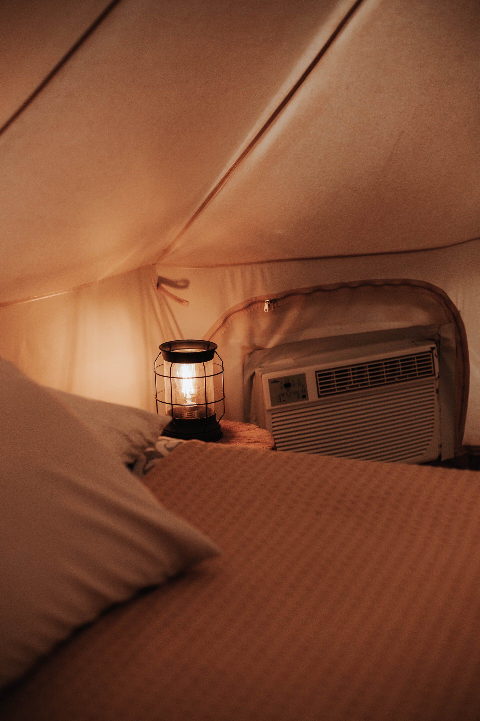 Close-up of a cozy bed inside a glamping tent, with soft lighting from a lantern, creating a warm and inviting atmosphere.