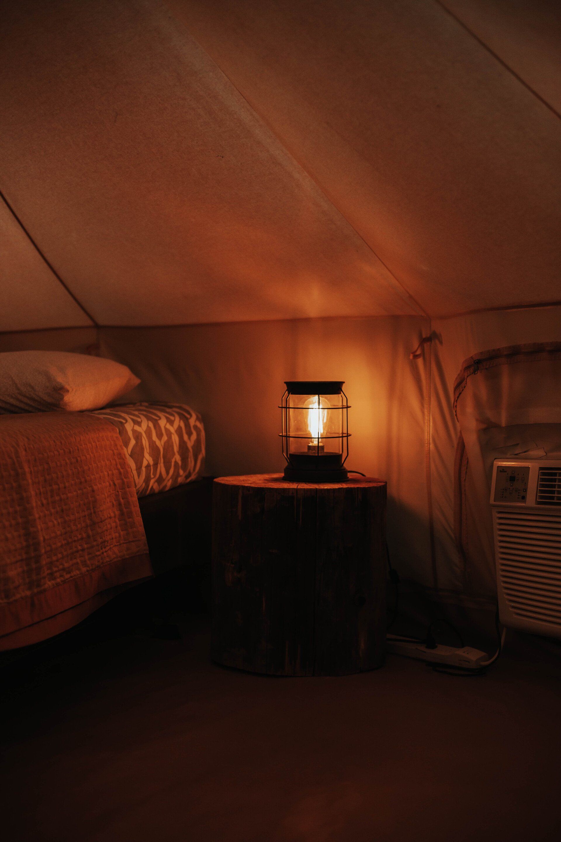 Warmly lit glamping tent interior featuring a comfortable bed, a rustic lantern, providing a relaxing and intimate setting