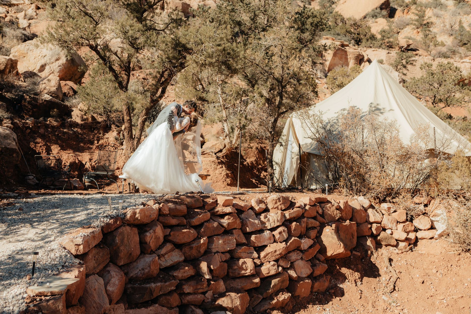 A married couple kiss outside their glamping tent, surrounded scenic landscapes, a picturesque setting for a wedding.

