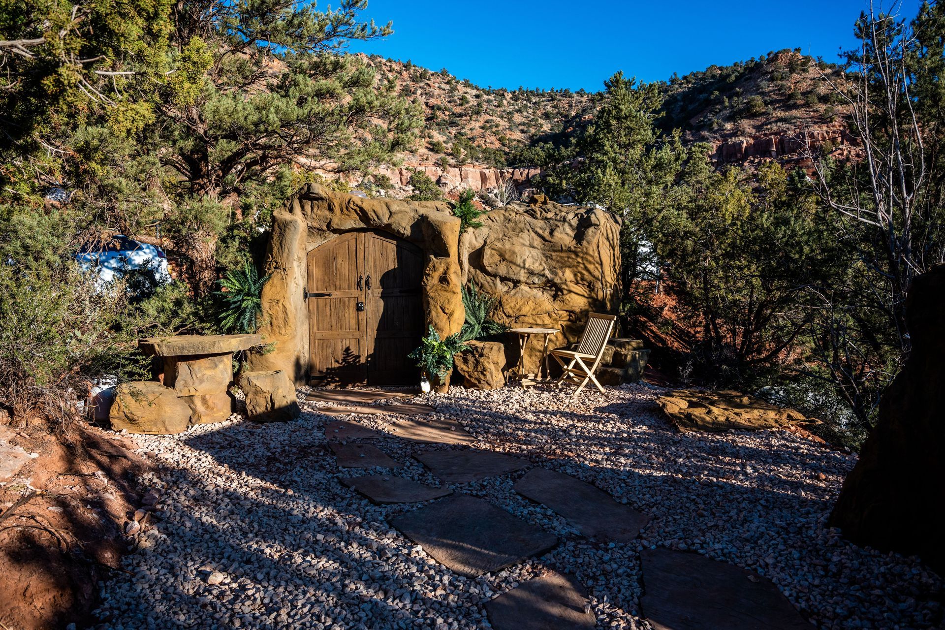 A rustic door set into a rock wall with chairs and a table outside, surrounded by nature near Zion Glamping Adventures.