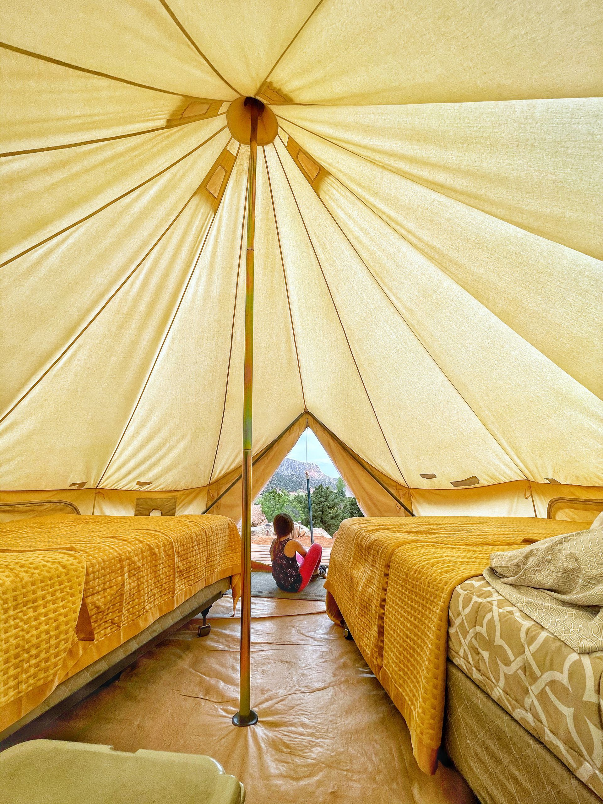 Glamping tent interior with two comfortable beds and a guest enjoying the scenic view, providing a relaxing environment.