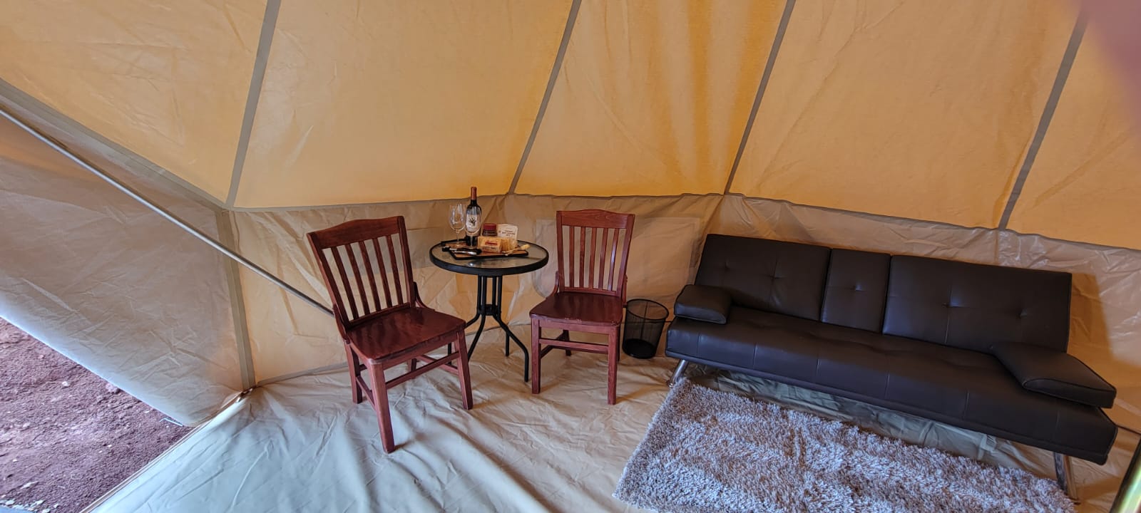 Glamping tent interior with a seating area including chairs and a table set with wine and snacks. Zion Glamping Adventures.