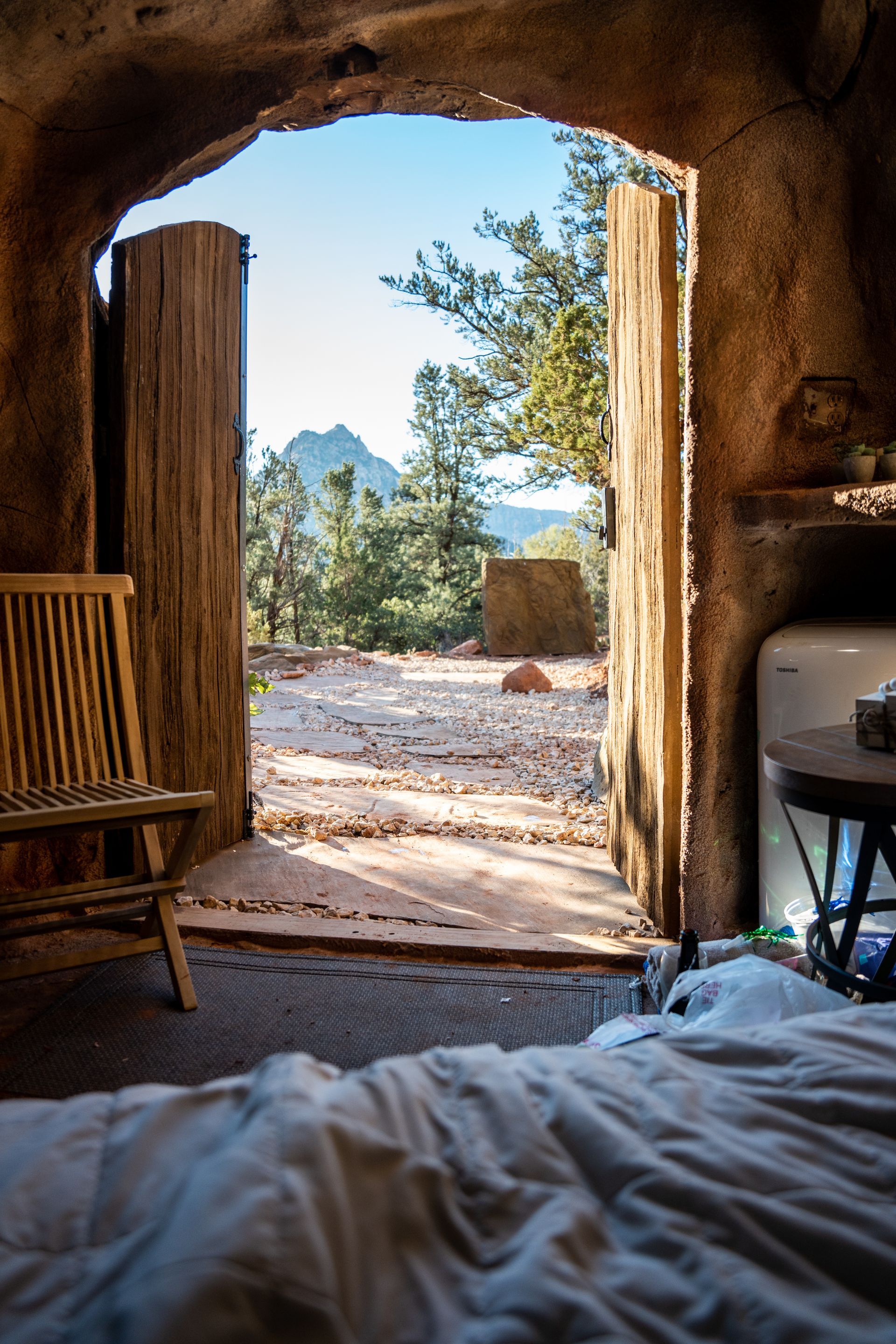 View from inside a cozy rock cabin looking out through an open wooden door at the natural scenery at Zion Glamping Adventures