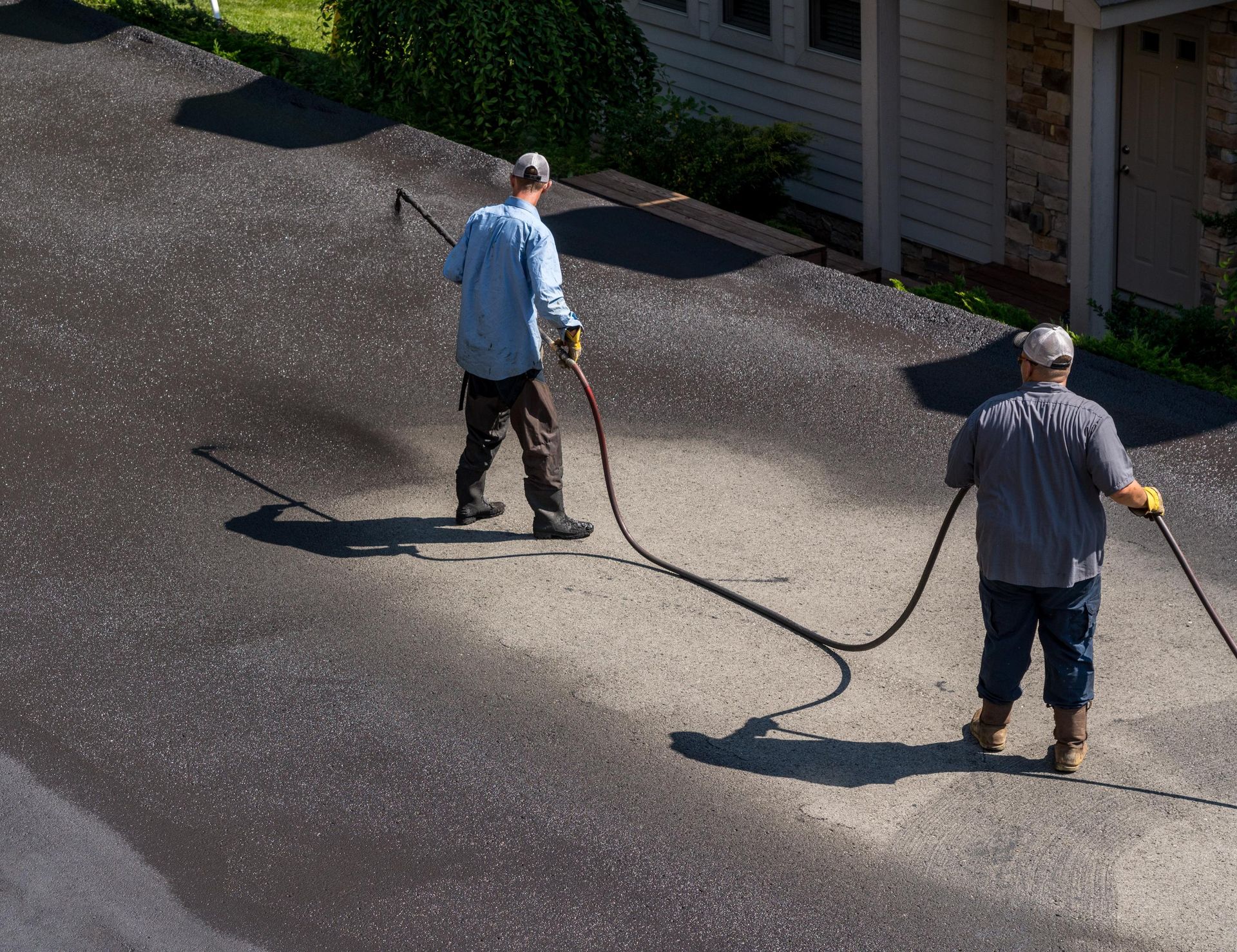 Two men are spraying asphalt on a driveway.