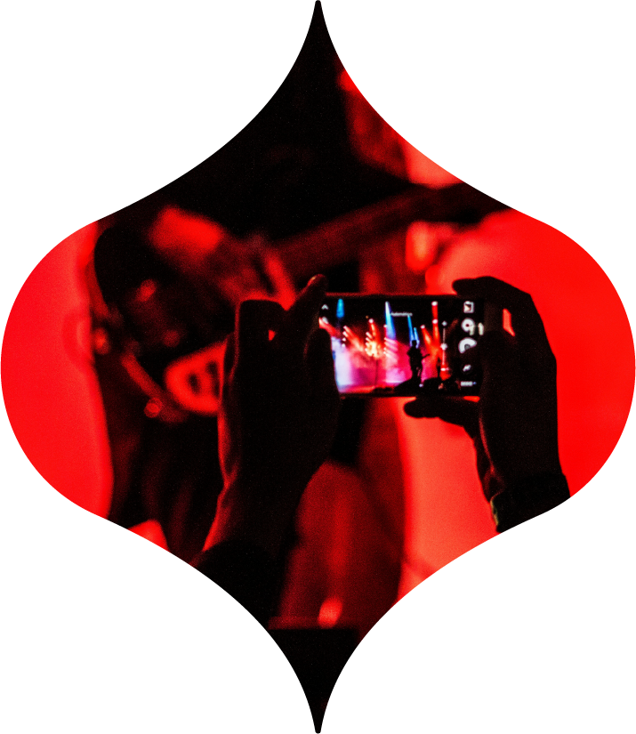 Hands holding a smartphone filming a red-lit concert stage