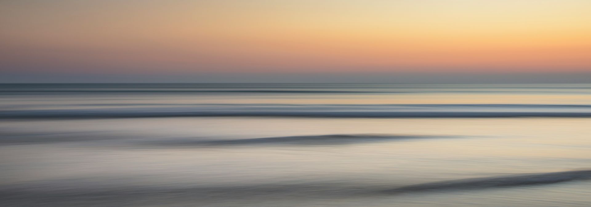 Calm beach at sunset with soft pastel sky and gentle waves washing ashore