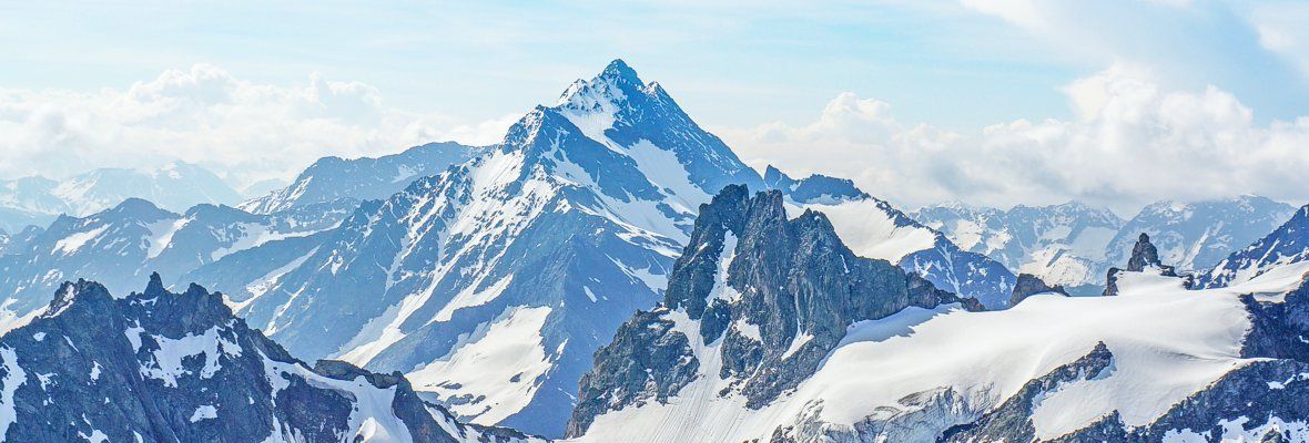 Snowy mountain peaks under a bright blue sky with wispy clouds