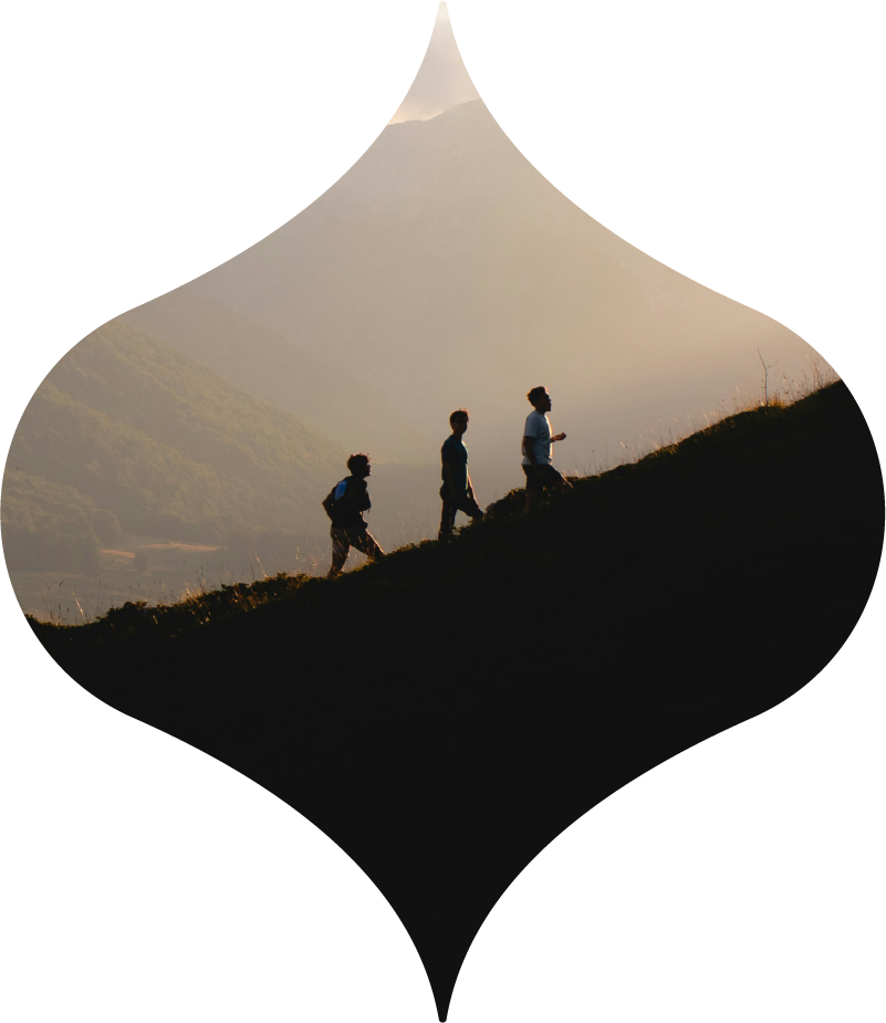 Three hikers silhouetted on a mountain ridge at sunset in a diamond-shaped frame