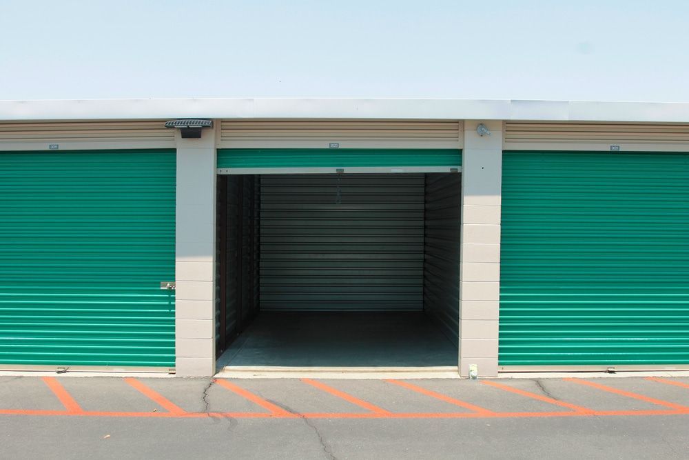 Three green storage units; one open, others closed. Exterior, concrete setting with blue sky. — Gympie Southside Mini Storage in Southside, QLD
