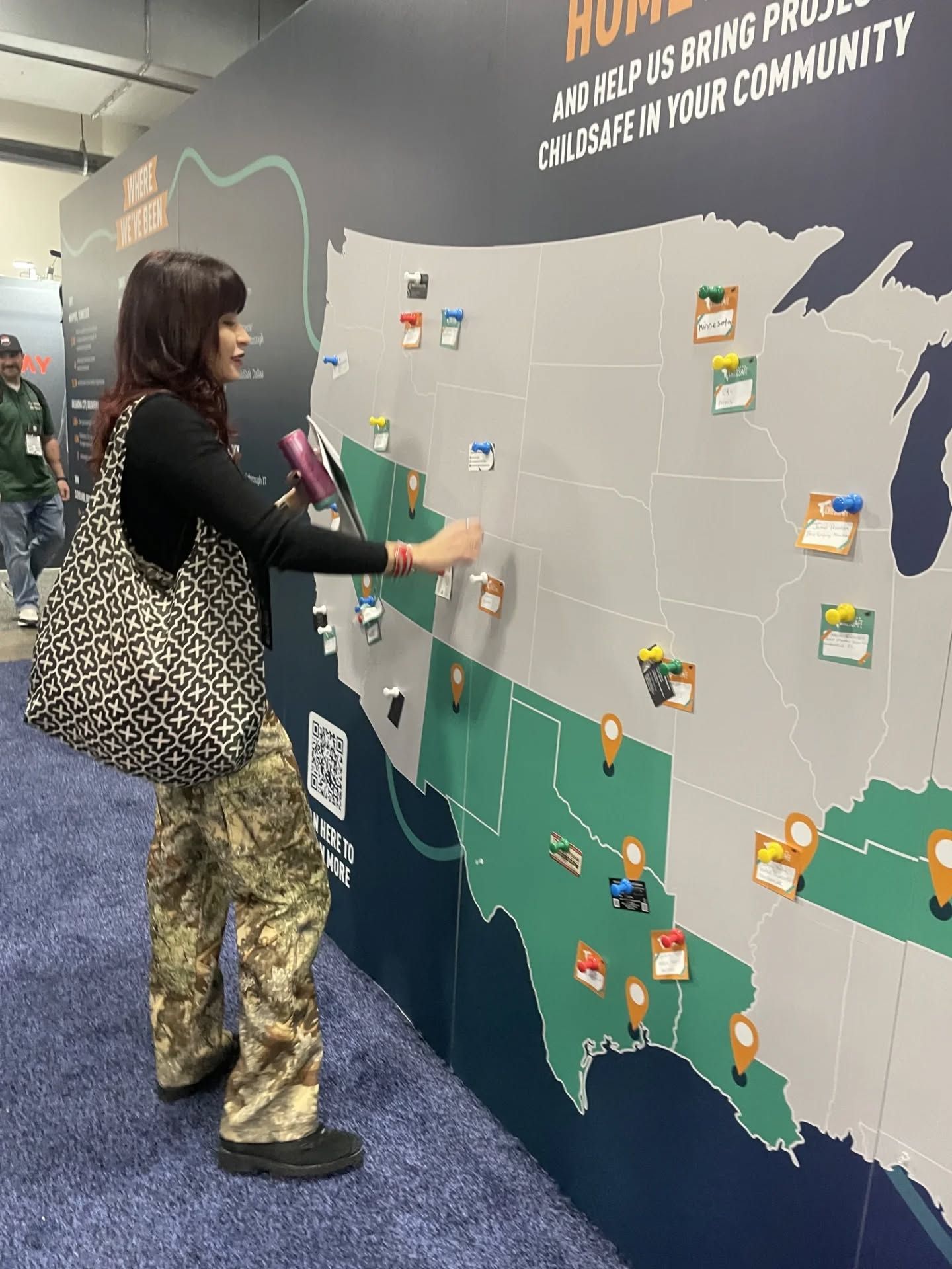 A person places a sticker on a large map of the United States displayed on a wall at an event.