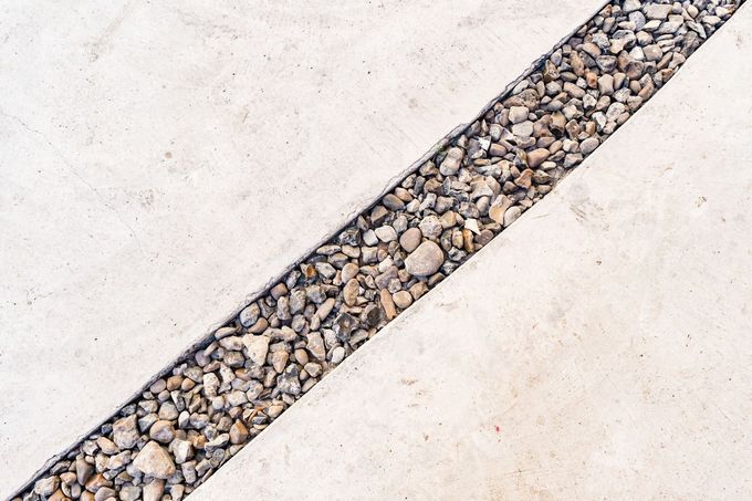 A diagonal strip of decorative grey and brown pebbles embedded in a smooth, light-colored concrete walkway.