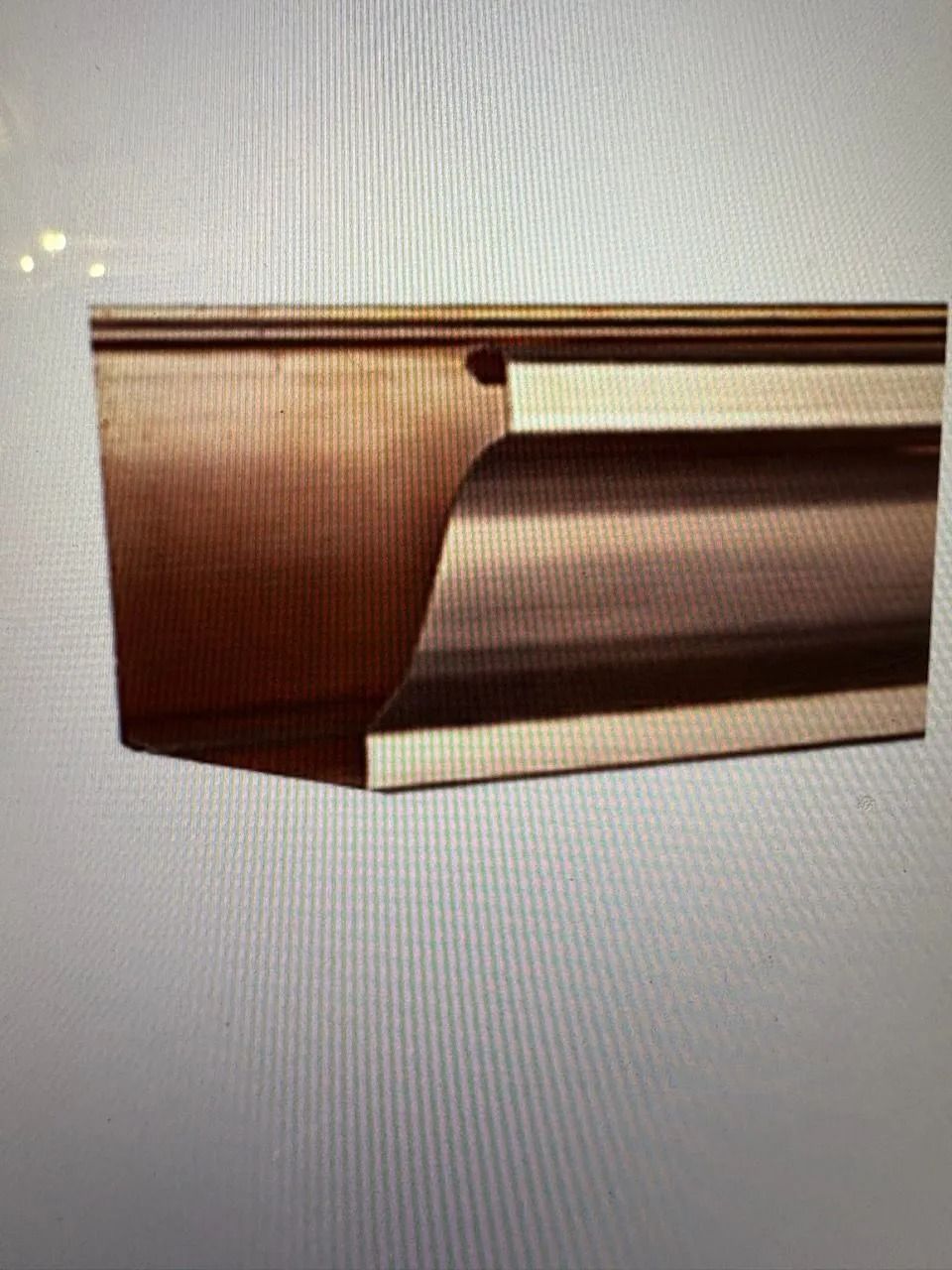 A cross-section view of a bronze-colored metal rain gutter, showing its curved decorative profile and flat back side.