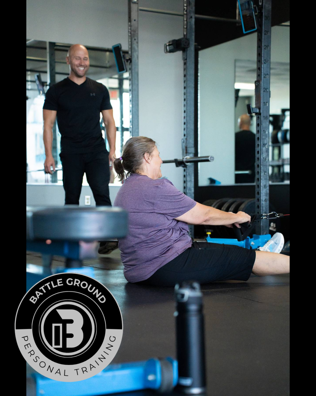 A woman seated on floor exercising with a cable machine; a trainer watches and smiles in gym. A woman seated on floor exercising with a cable machine; a trainer watches and smiles in gym.