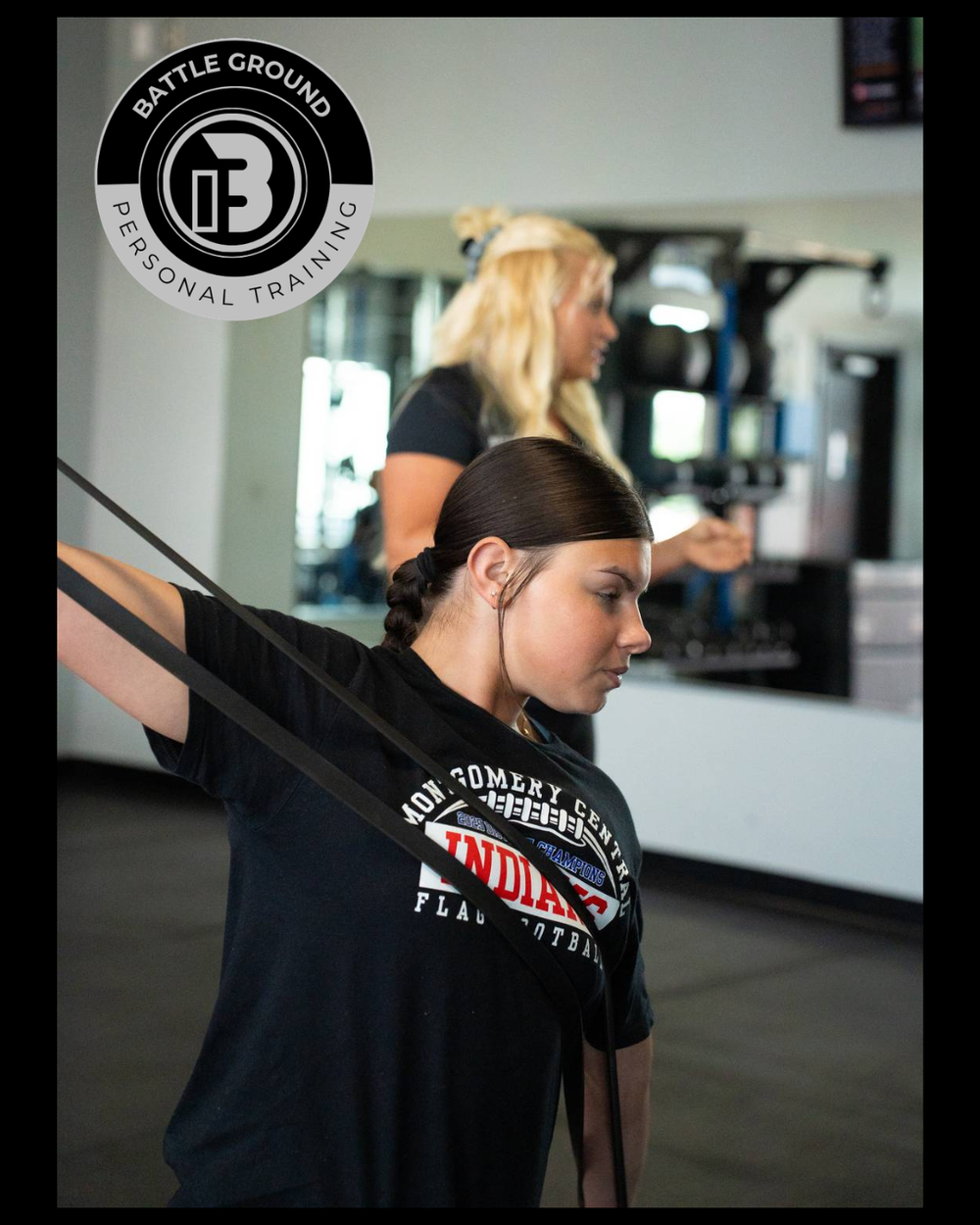 Woman using resistance band for exercise; instructor watches in gym setting. Woman using resistance band for exercise; instructor watches in gym setting.