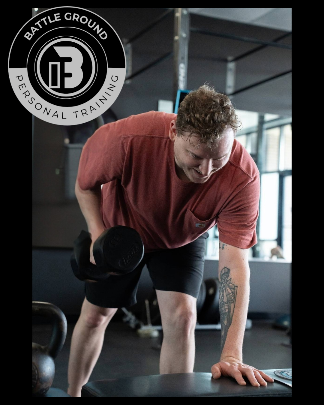 Man lifting dumbbell in a gym. Red shirt, black shorts. Holding weight, focused expression. Battle Ground logo. Man lifting dumbbell in a gym. Red shirt, black shorts. Holding weight, focused expression. Battle Ground logo.