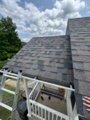 Gray shingled roof with ladder and gutter against a cloudy sky