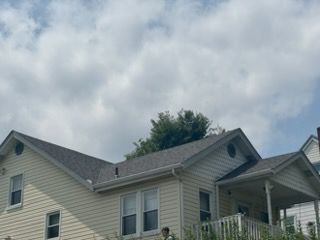 Two-story beige house with gray roof and front porch under a cloudy sky