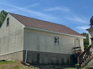Side view of a gray house with a sloped roof, small window, and staircase on the right.