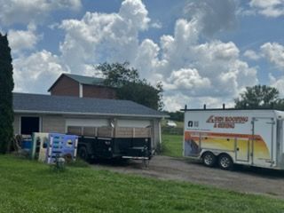 Moving truck parked beside a house on a cloudy day, with a black pickup under the carport.