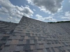 Gray shingled roof under a cloudy sky, with a raised ridge section in the center