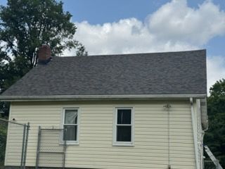 Side view of a beige house with a gray shingled roof and white-framed windows under a cloudy sky