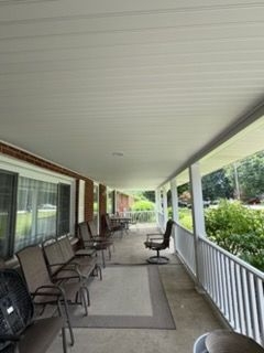 Covered front porch with chairs, railing, and potted plants along a house exterior