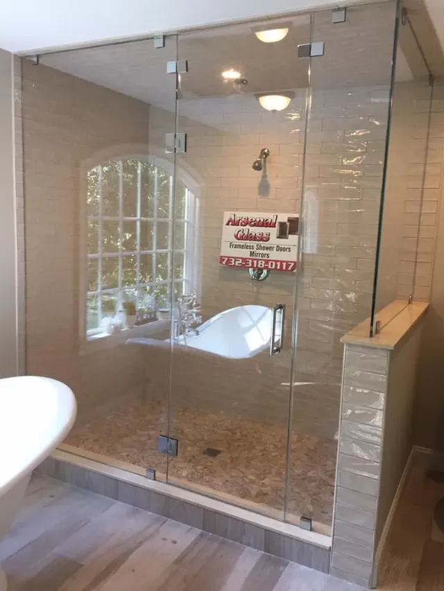 Large custom frameless glass shower enclosure with a pebble floor and tan subway tile, expertly installed by Arsenal Glass.