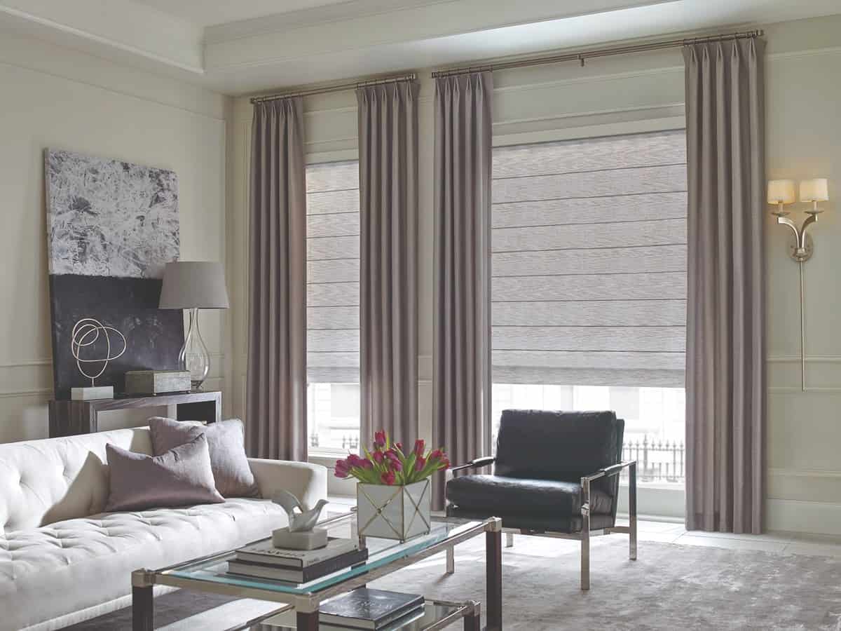 A living room with drapery and architectural roller shades.