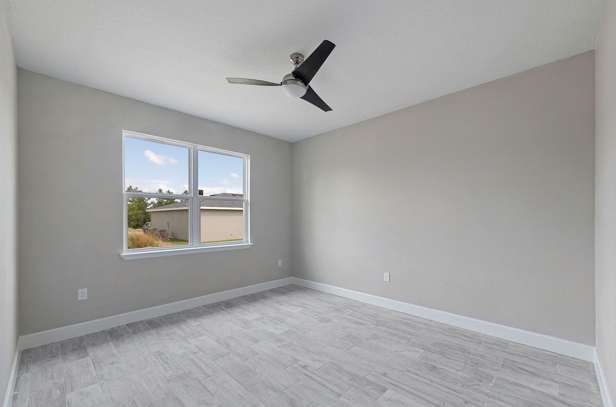 An empty bedroom with a ceiling fan and two windows.
