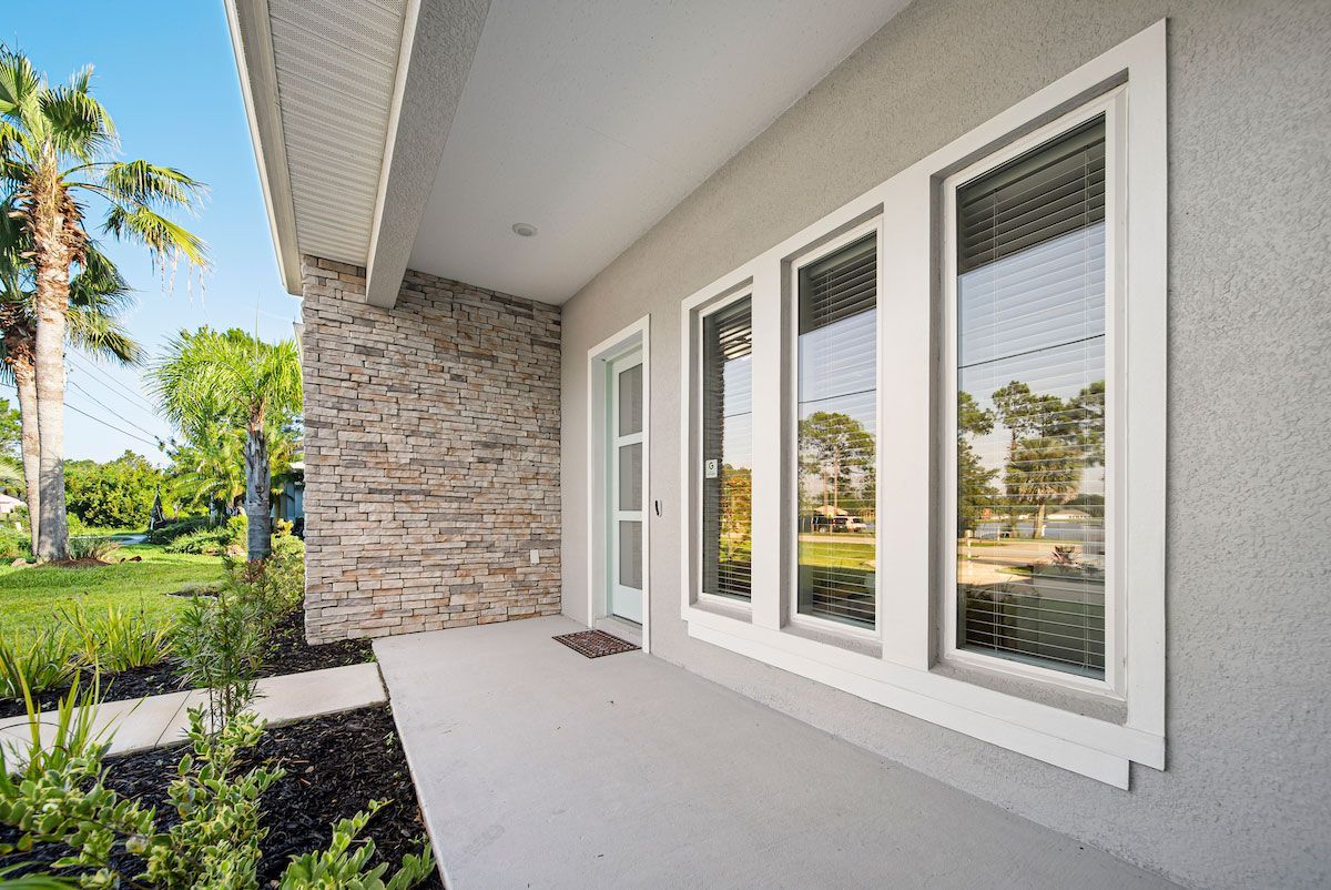 The front porch of a house with three windows and a stone wall.