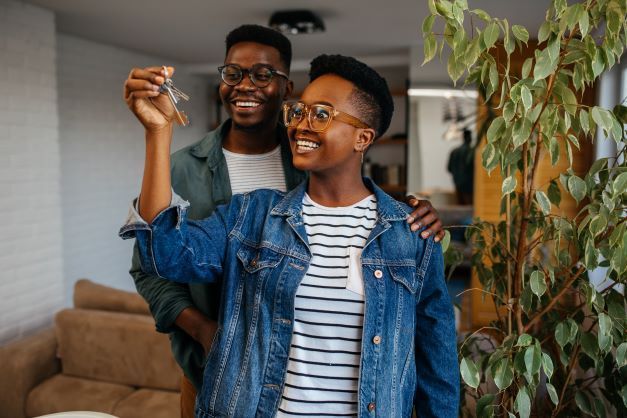 A man and a woman are standing in a living room holding keys to their new home.