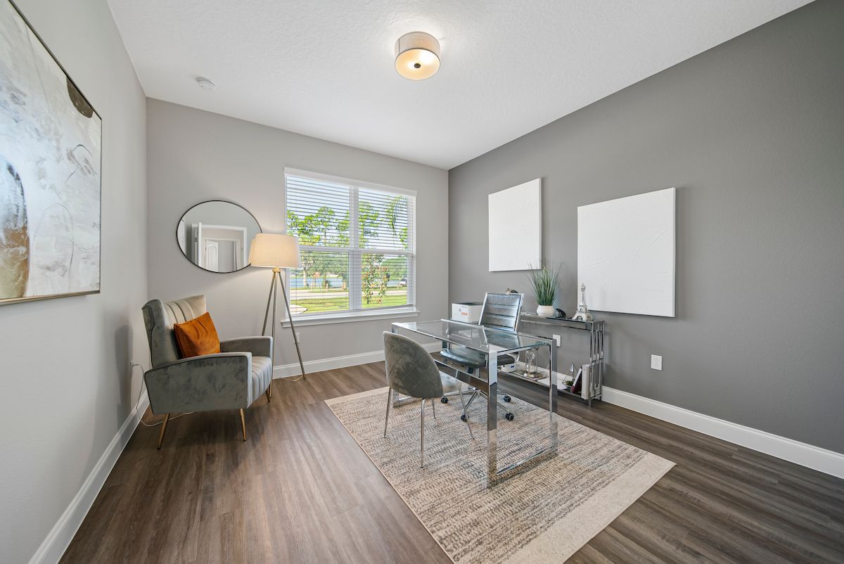 A home office with a desk , chairs , and a large window.
